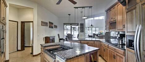 A spacious kitchen with wooden cabinets, a granite countertop island, a ceiling fan, and a large window providing natural light.