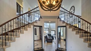 A grand staircase with ornate railings, leading to a spacious living area with a large window and a fireplace. - Resort Style Family Fun with Guest House (Brighton)