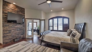 A bedroom with a bed, a ceiling fan, a TV mounted on the wall, and a large window. - Resort Style Family Fun with Guest House (Brighton)