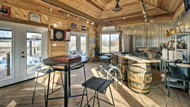 A rustic interior with wooden beams, a bar area with stools, a dartboard, and a kitchen with a metal shelf. - Resort Style Family Fun with Guest House (Brighton)