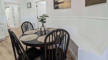 A dining area with a round table, black chairs, a potted plant, a painting, and a wooden panel on the wall.