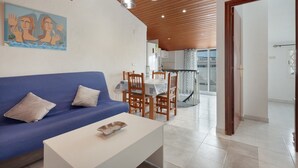 Een moderne woonkamer met een blauwe bank, een witte salontafel, houten eetkamerstoelen en hanglampen.