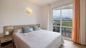 Een hotelkamer met een bed, nachtkastje, lamp en uitzicht op een balkon met tuinmeubilair.