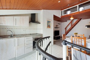 A kitchen with white cabinets, a stainless steel range hood, and a dining area with a wooden table and chairs. - Apartment 'Dúplex Salou' with Shared Pool, Wi-Fi and Air Conditioning (Salou)