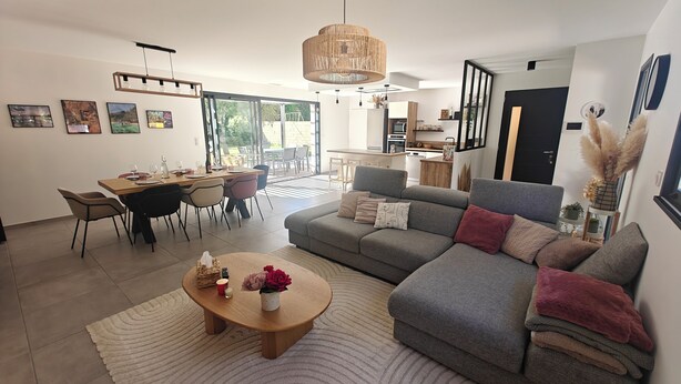 A modern living room with a sofa, coffee table, dining table, and chairs. There is a kitchen area in the background. - CASA NUBA - Modern villa with Jacuzzi - Between Provence & Mont Ventoux (Carpentras)