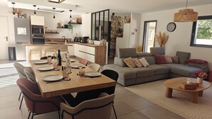 A modern kitchen with a dining area, a grey sofa, and a small round table with a vase. - CASA NUBA - Modern villa with Jacuzzi - Between Provence & Mont Ventoux (Carpentras)
