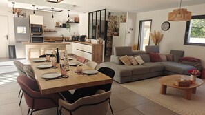 A modern kitchen with a dining area, a grey sofa, and a small round table with a vase. - CASA NUBA - Modern villa with Jacuzzi - Between Provence & Mont Ventoux (Carpentras)