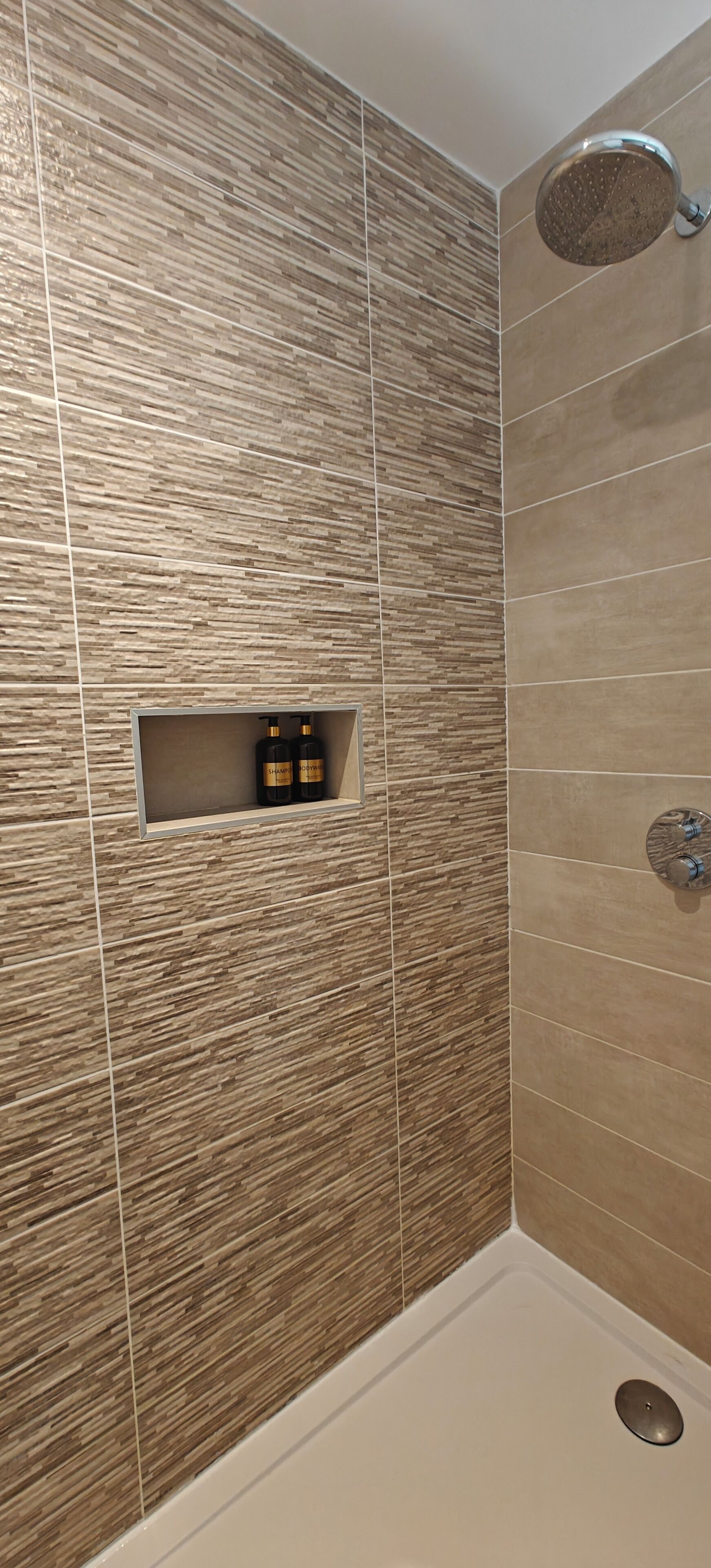 Un espace douche doté d’une douche à pluie, d’une étagère intégrée pour les articles de toilette et d’un drain.