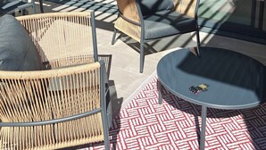 A modern outdoor seating area with wicker furniture and a patterned rug, a glass door leading to a kitchen, and a view of greenery. - CASA NUBA - Modern villa with Jacuzzi - Between Provence & Mont Ventoux (Carpentras)