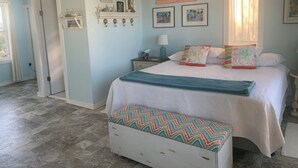 Un dormitorio con cama, mesita de noche, cómoda, ventana con cortinas y adornos en la pared.