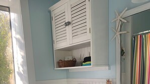 Un baño con inodoro, lavamanos, un cuadro enmarco y una ventana con toallas.