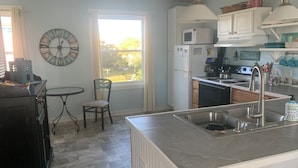 Una cocina con una isla central, una mesa de comedor, un reloj y vistas al exterior.