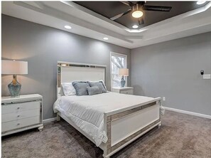 Un dormitorio con cama, mesitas de noche, ventana y ventilador de techo.