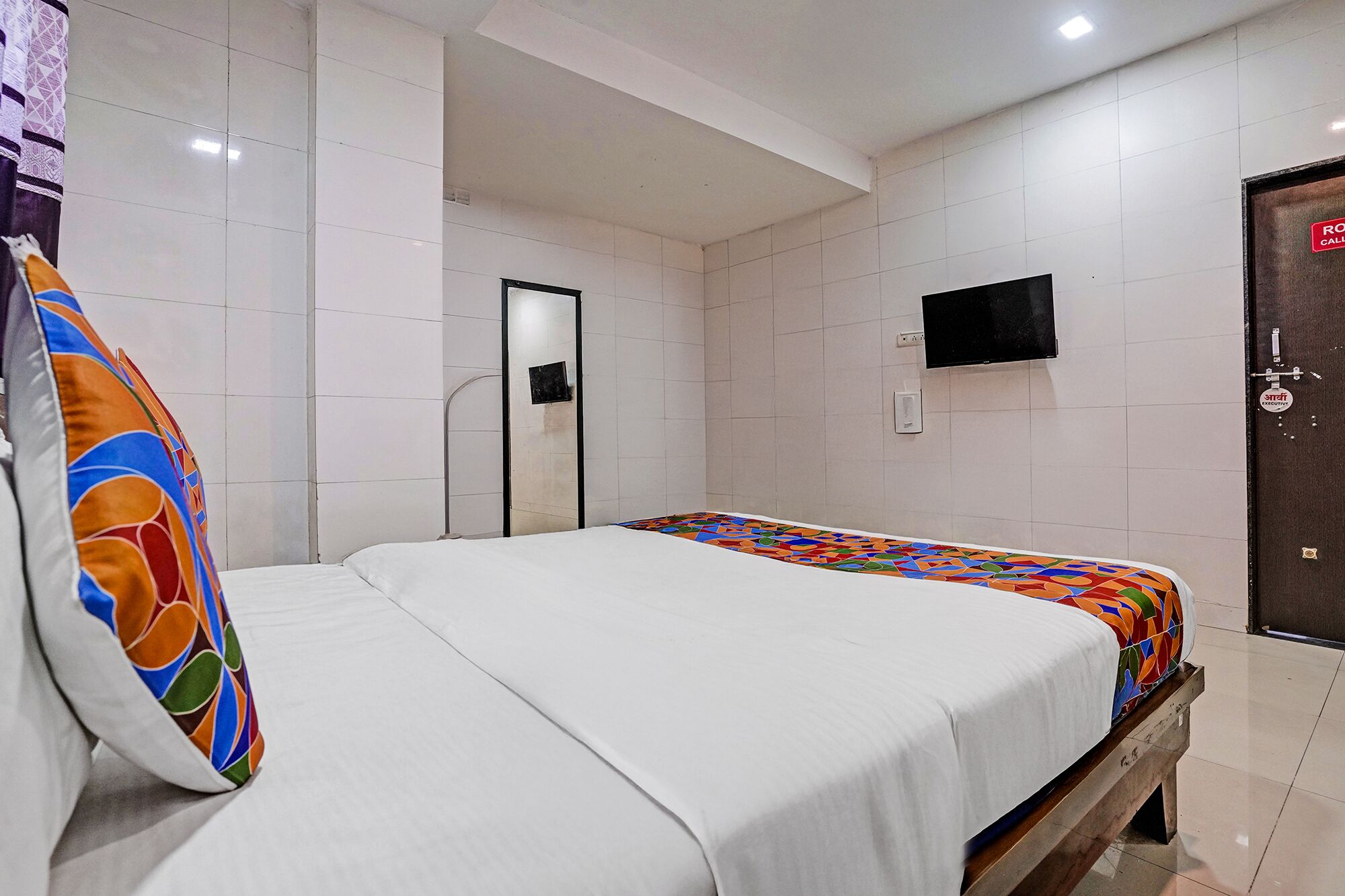 A hotel room with a bed, a TV mounted on the wall, and a door with a sign.