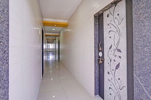 Un pasillo con paredes de azulejos blancos, una puerta tipo mármol con un panel decorativo e iluminación empotrada en el techo.