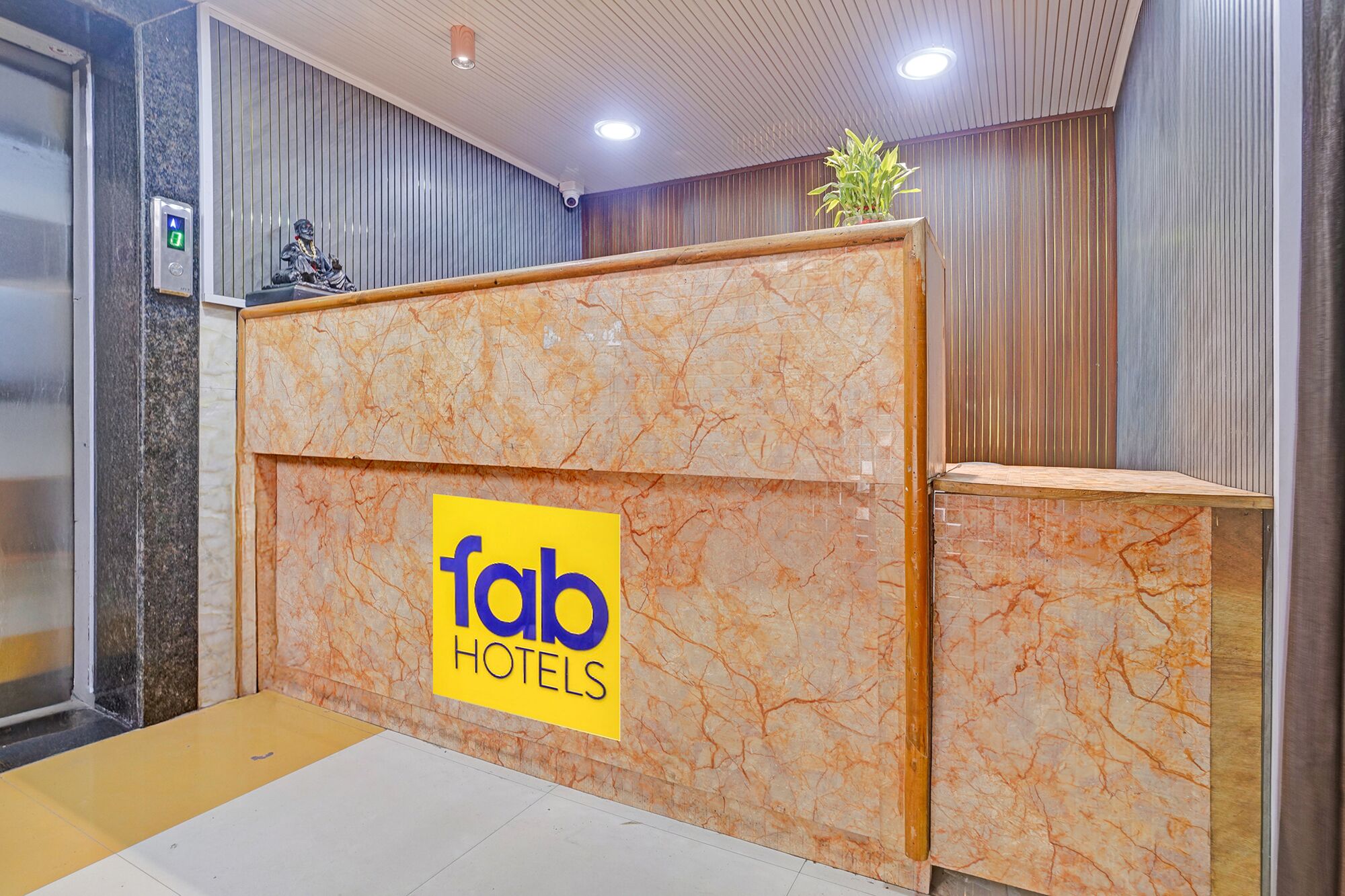 Un comptoir d’accueil avec un revêtement en marbre, une enseigne indiquant « fab hotels », et une petite plante posée sur le dessus.