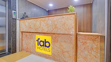 Un comptoir d’accueil avec un revêtement en marbre, une enseigne indiquant « fab hotels », et une petite plante posée sur le dessus.
