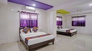 Habitación de hotel con dos camas, cortinas moradas, paredes con azulejos blancos y un ventilador de techo.