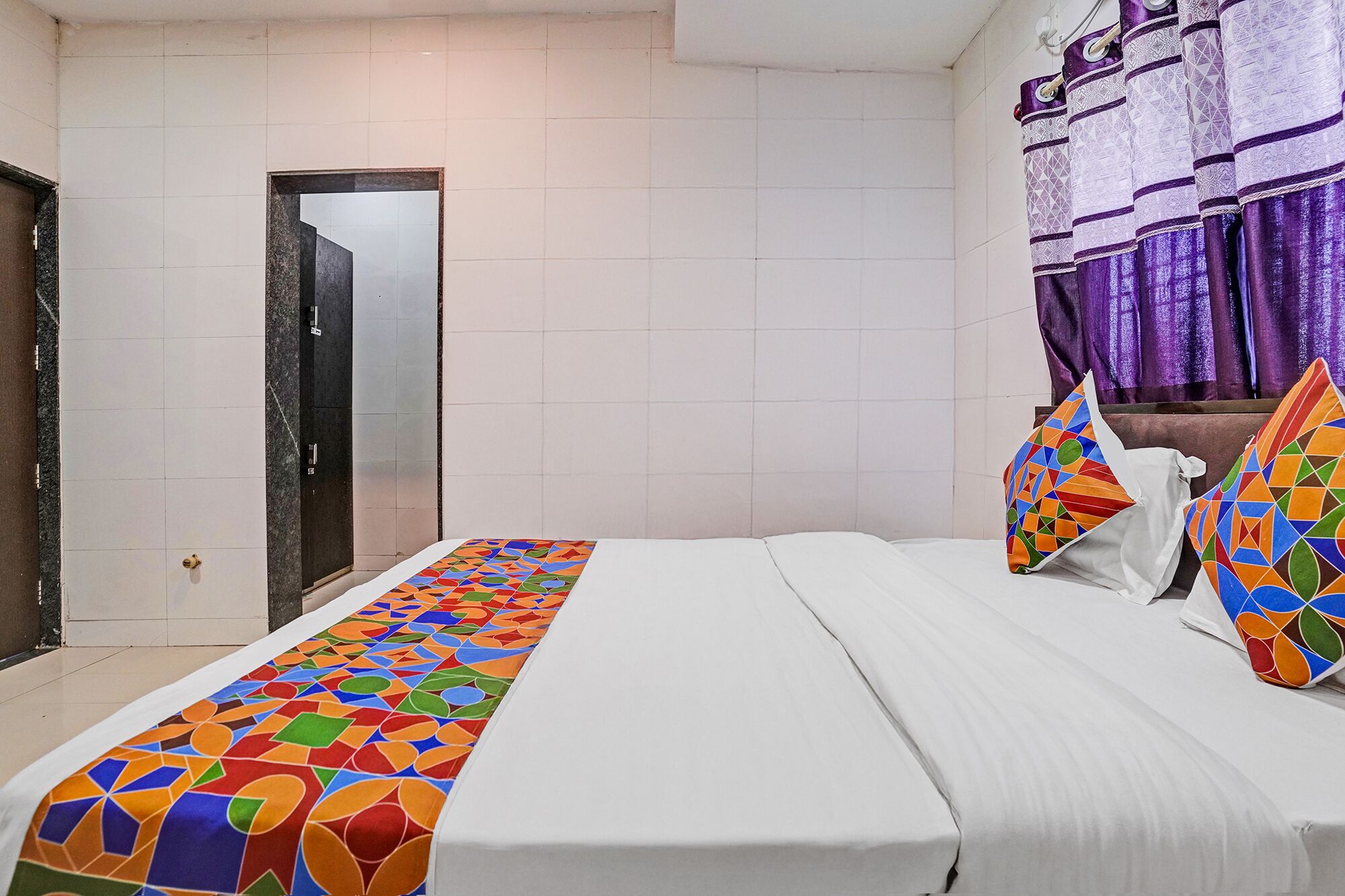 Una habitación de hotel con una cama, una puerta y un ventanal con cortinas moradas.