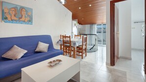 A modern living room with a blue sofa, white coffee table, wooden dining table with chairs, and pendant lighting. - 'Sobreático Salou' Apartment with Shared Pool, Wi-Fi, and Air Conditioning (Salou)