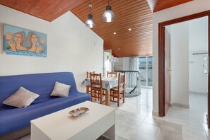 A modern living room with a blue sofa, white coffee table, wooden dining table with chairs, and pendant lighting. - 'Sobreático Salou' Apartment with Shared Pool, Wi-Fi, and Air Conditioning (Salou)