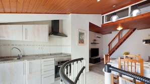 A kitchen with white cabinets, a stainless steel range hood, and a dining area with a wooden table and chairs. - 'Sobreático Salou' Apartment with Shared Pool, Wi-Fi, and Air Conditioning (Salou)