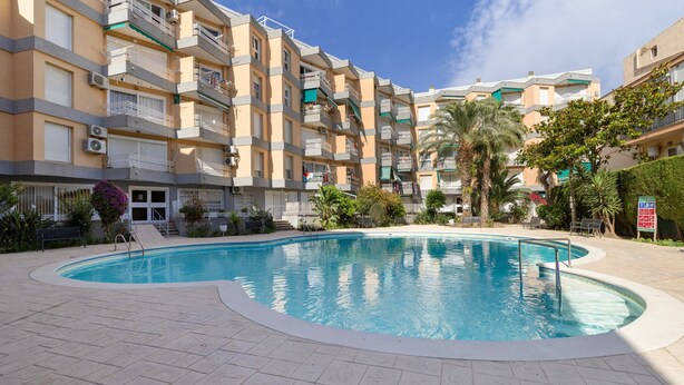 A swimming pool with a tiled deck, surrounded by multi-story residential buildings with balconies and air conditioning units. - 'Sobreático Salou' Apartment with Shared Pool, Wi-Fi, and Air Conditioning (Salou)