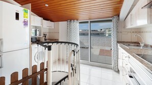 A kitchen with a wooden ceiling, a refrigerator, a sink, and a view through a glass door. - 'Sobreático Salou' Apartment with Shared Pool, Wi-Fi, and Air Conditioning (Salou)