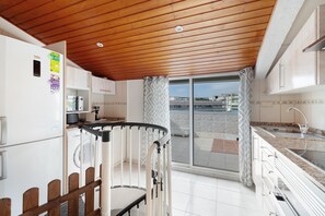 A kitchen with a wooden ceiling, a refrigerator, a sink, and a view through a glass door. - 'Sobreático Salou' Apartment with Shared Pool, Wi-Fi, and Air Conditioning (Salou)