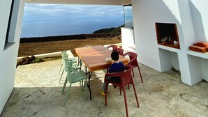 Zona pranzo esterna moderna con vista sul mare, un tavolo in legno e sedie rosse.