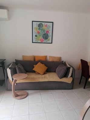 Una sala de estar con un sofá, una mesa redonda de madera, una obra de arte floral enmarco y una silla.