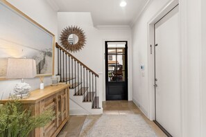 A hallway with a wooden staircase, a mirror, a framed picture, and a door leading to another room. - Luxury Resort Home w/ Two Golf Carts (Miramar Beach)