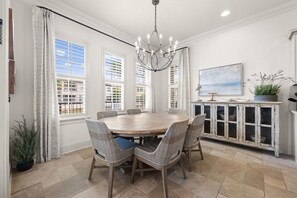 A dining room with a round table, wicker chairs, a chandelier, and a cabinet with glass doors. - Luxury Resort Home w/ Two Golf Carts (Miramar Beach)