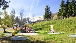 Un parque con juegos infantiles, césped y una colina.
