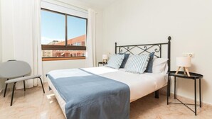 A hotel room with a bed, a chair, a nightstand, and a window with a view. - Las Olas (El Médano)