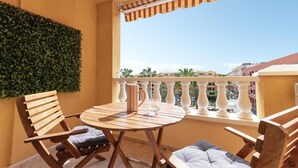 A balcony with a view of buildings, a round wooden table, two wooden chairs, a striped mug, and a white lamp. - Las Olas (El Médano)