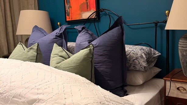 A neatly made bed with a white quilt, a blue wall with two paintings, and a lamp on a bedside table. - House Sleeps 2 With Parking (London)