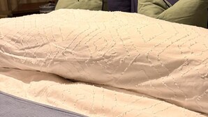 A bed with a textured white duvet, a grey mattress cover, and multiple pillows in various colors. - House Sleeps 2 With Parking (London)