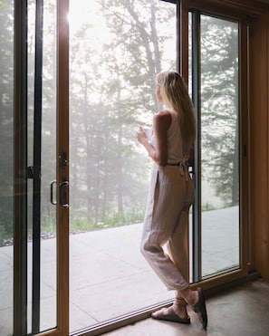 A person standing at a glass door with a view of trees outside.