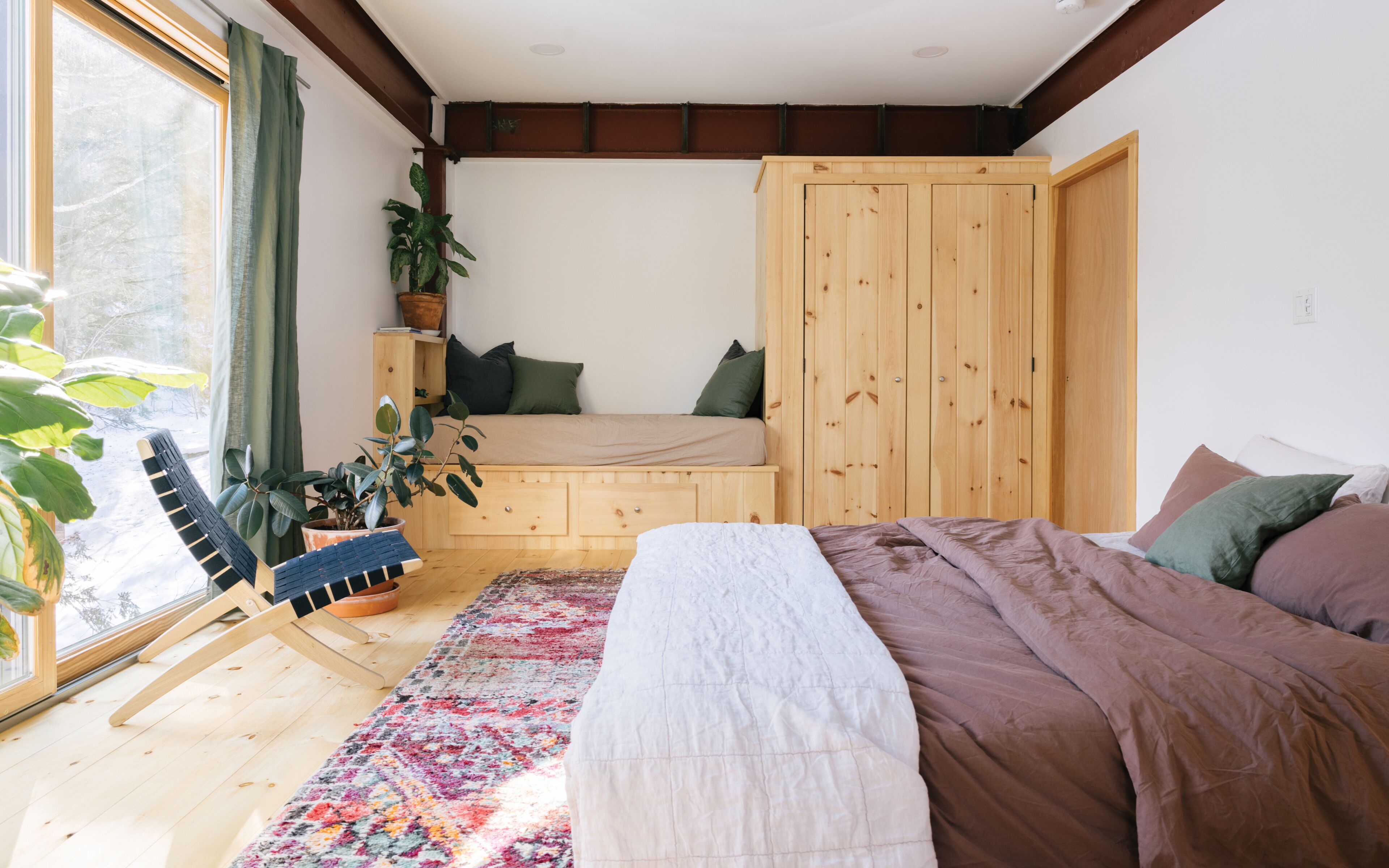 A bedroom with a bed, a bench, a window, and a plant.