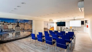 Un salón de conferencias con sillas azules, una pantalla de proyector y un gran mural de un paisaje urbano.