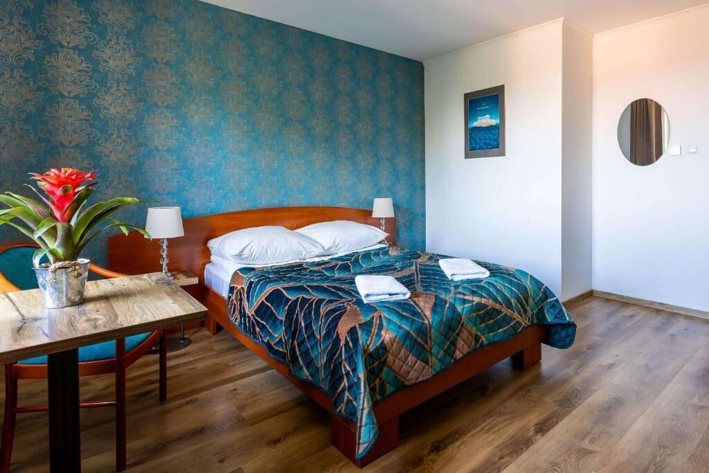 A hotel room with a bed, a table with a plant, a lamp, and a painting on the wall.