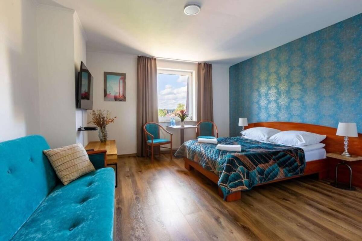 A hotel room with a bed, a blue sofa, a small table, and a window with curtains.