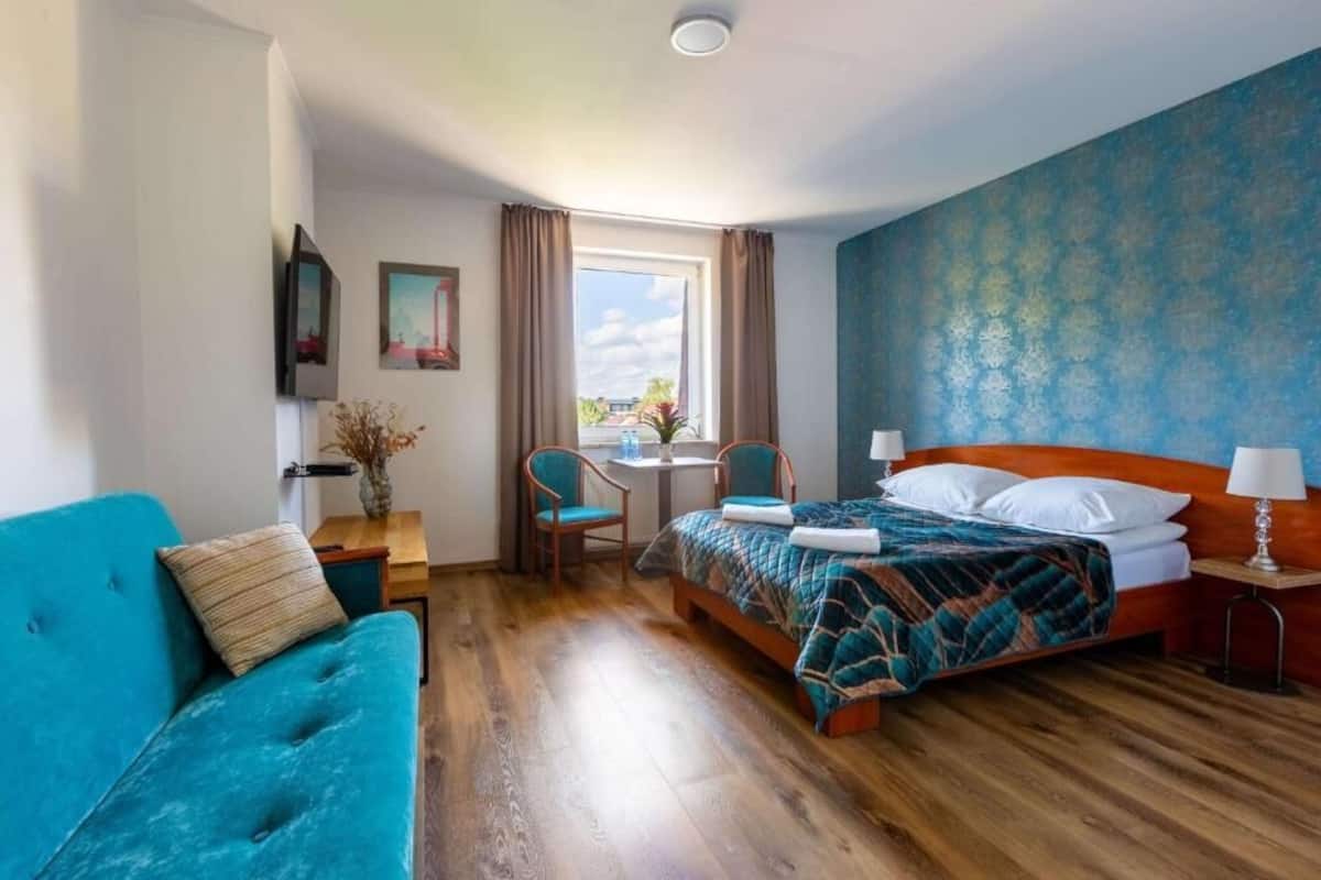 Ein Hotelzimmer mit einem Bett, einem blauen Sofa, einem kleinen Tisch und einem Fenster mit Vorhängen.