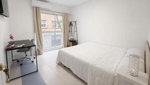 Un dormitorio con cama, escritorio, silla, lámpara colgante y ventana con cortinas.