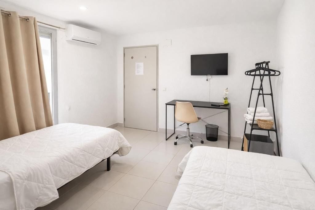 A hotel room with two beds, a desk, a chair, a TV, and a clothes drying rack.