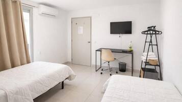 Hotellihuone, jossa on kaksi sänkyä, työpöytä, tuoli, televisio ja pyykiteline.