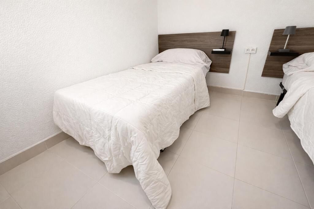 A single bed with a wooden headboard, a bedside table with a lamp, and a wall socket.