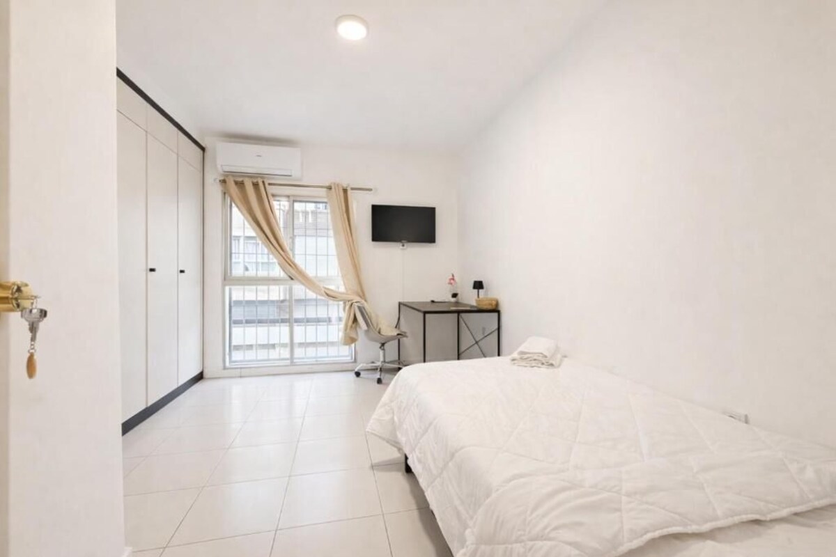 Un dormitorio con una cama, un escritorio, una silla, un televisor y una ventana con cortinas.