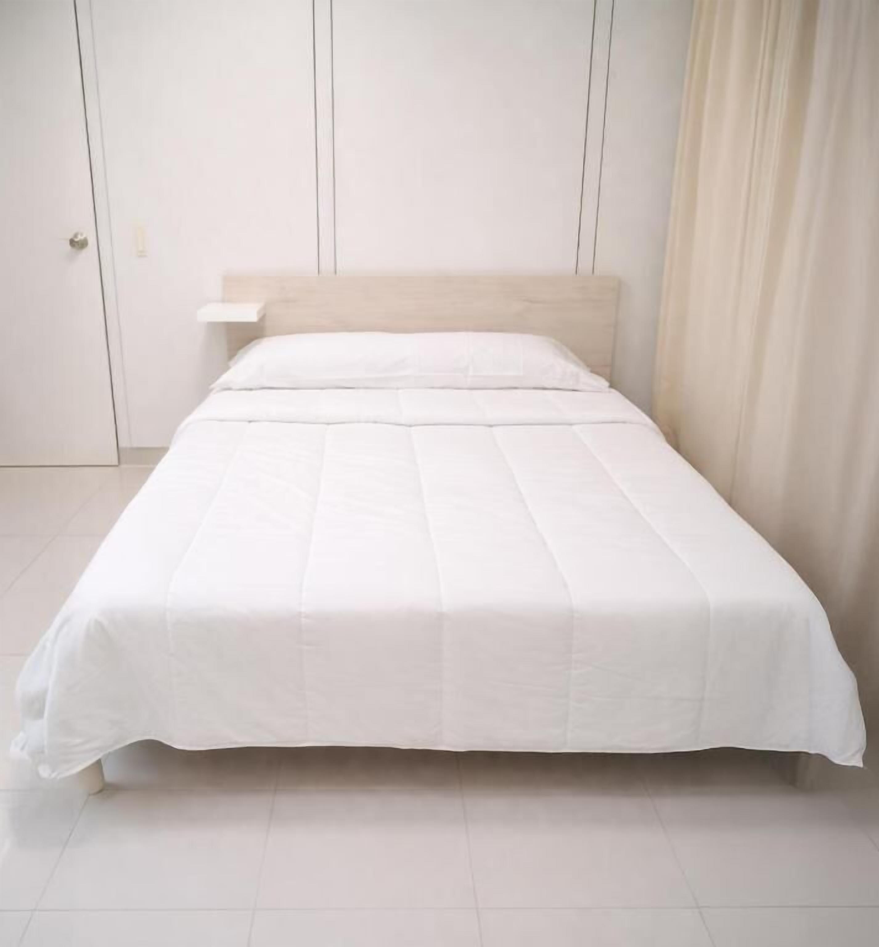 Una cama con colchón y cabecera blancos, una pared blanca y una puerta.